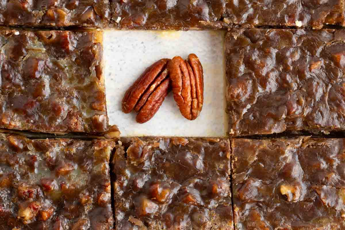 cut pecan pie bars with one cut out of the middle, and 2 whole pecans laying in its place