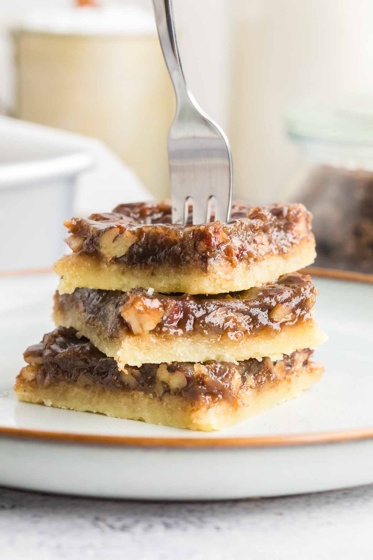 3 stacked pecan pie bars on white plate with metal fork going into the middle