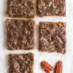 5 pecan pie bars on paper with a couple pecans laying next to it