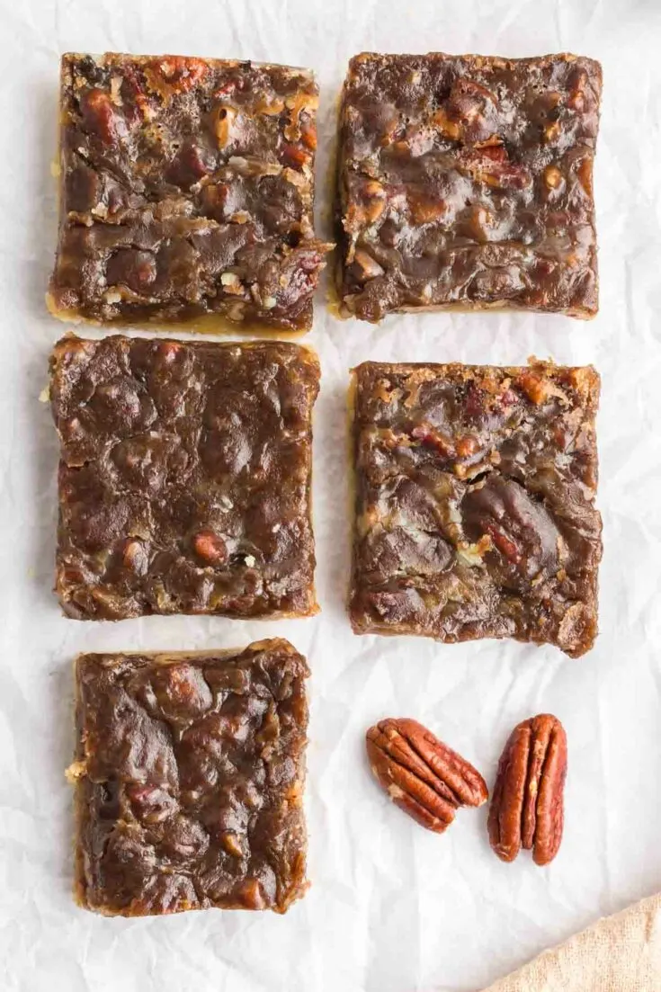 5 pecan pie bars on paper with a couple pecans laying next to it