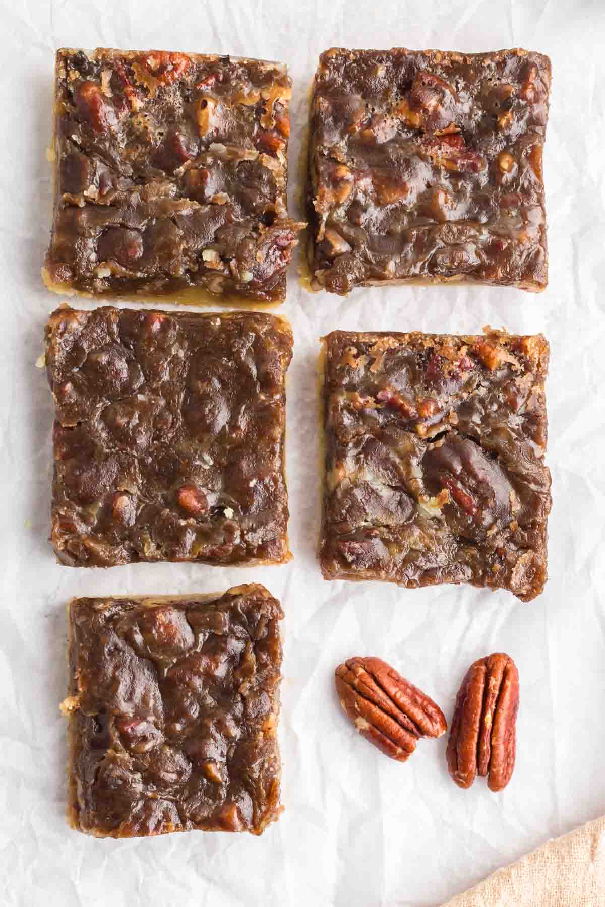 5 pecan pie bars on paper with a couple pecans laying next to it