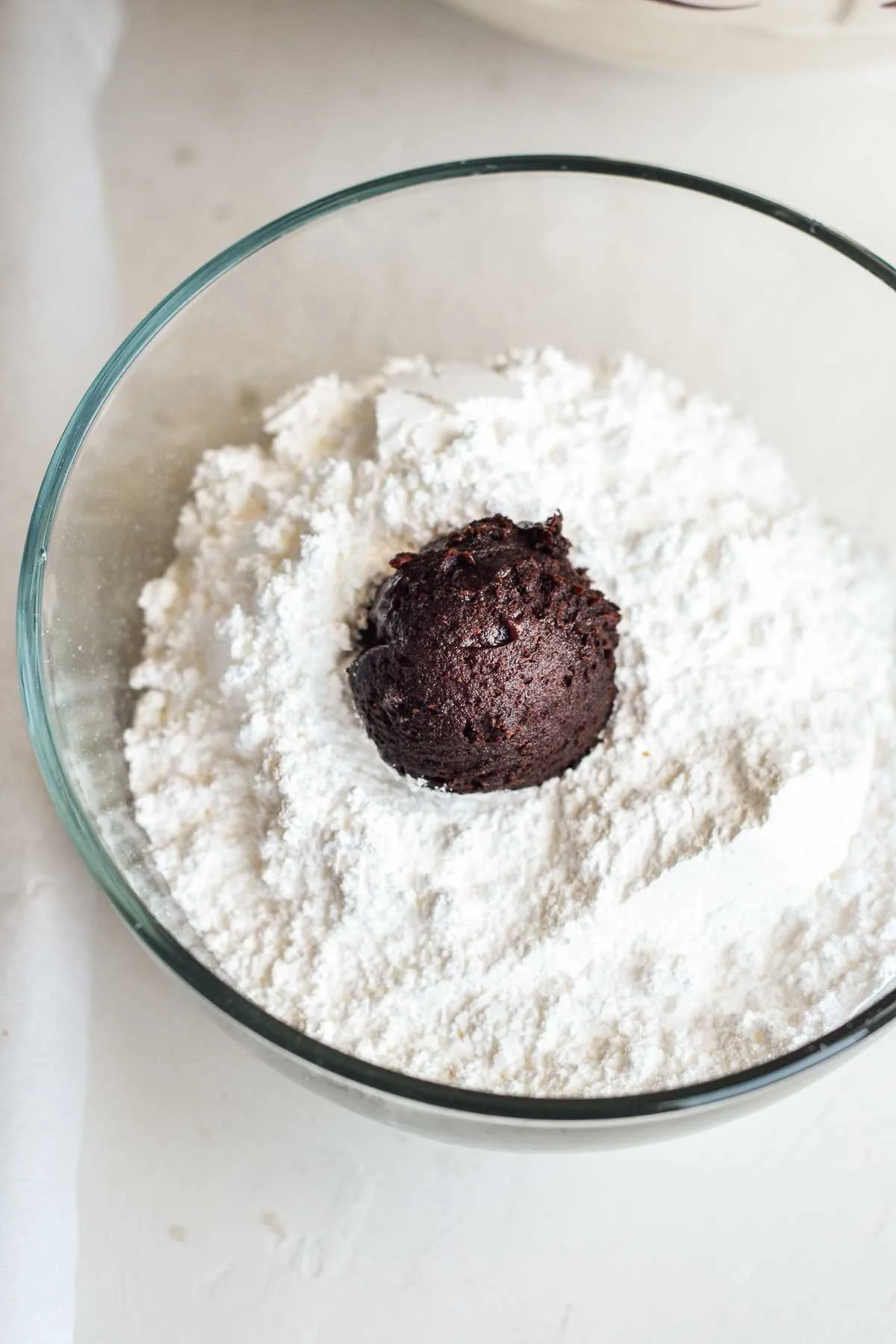 chocolate cookie dough ball in a clear bowl of powdered sugar