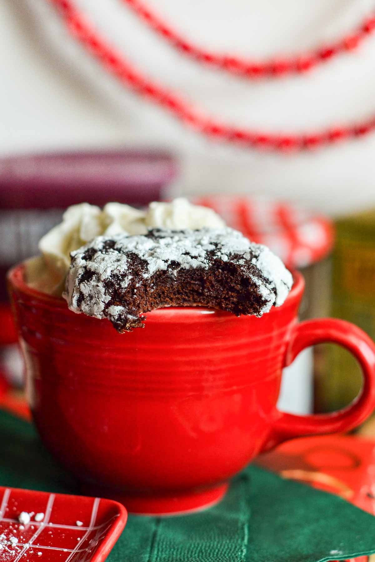 a bitten chocolate crinkle cookie sitting on top of a red coffee mug