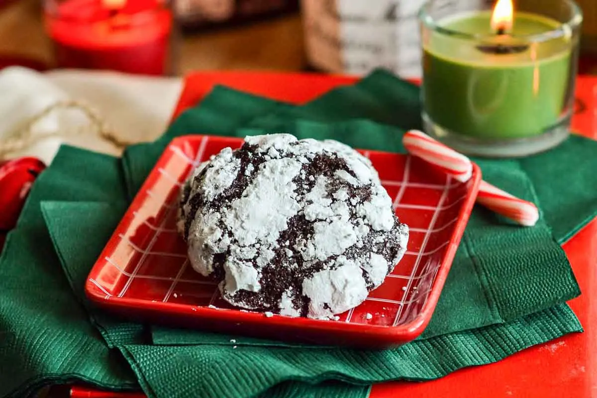 Raspberry Chocolate Crinkle Cookie on a red checkered plate on top of green napkins and a lit green candle in the bakground