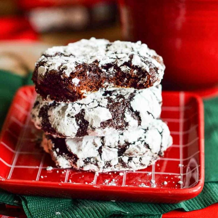 stack of Raspberry Chocolate Crinkle Cookies on a red checkered plate with a bite taken out of the top cookie