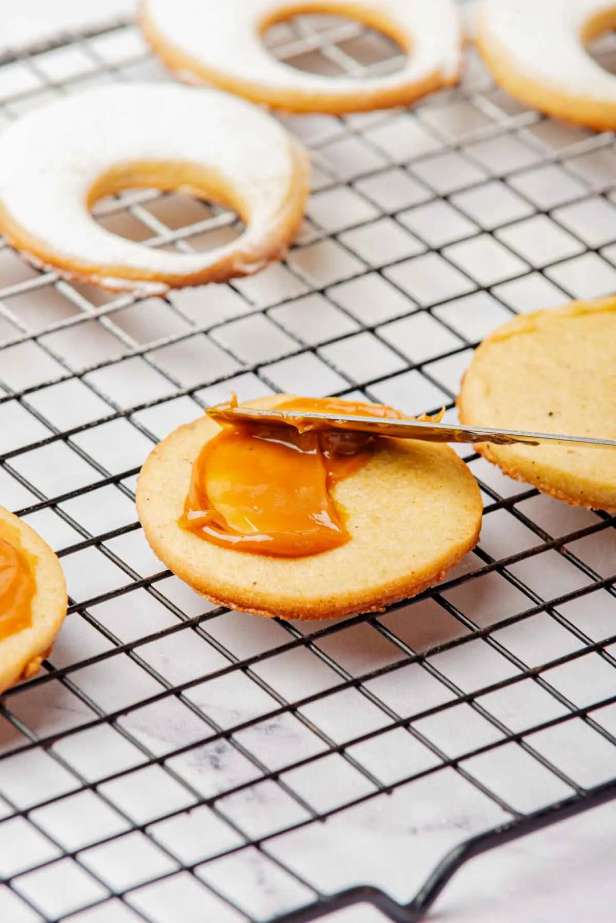 spreading caramel sauce on the linzer cookie which is on a wire rack