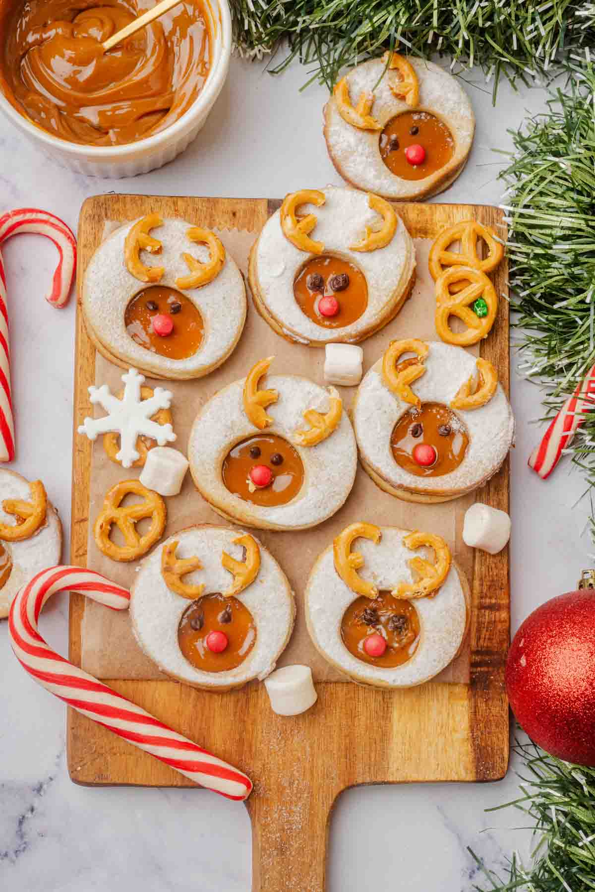 7 Rudolph Reindeer Linzer Cookies on wooden cutting board with Christmas decorations around