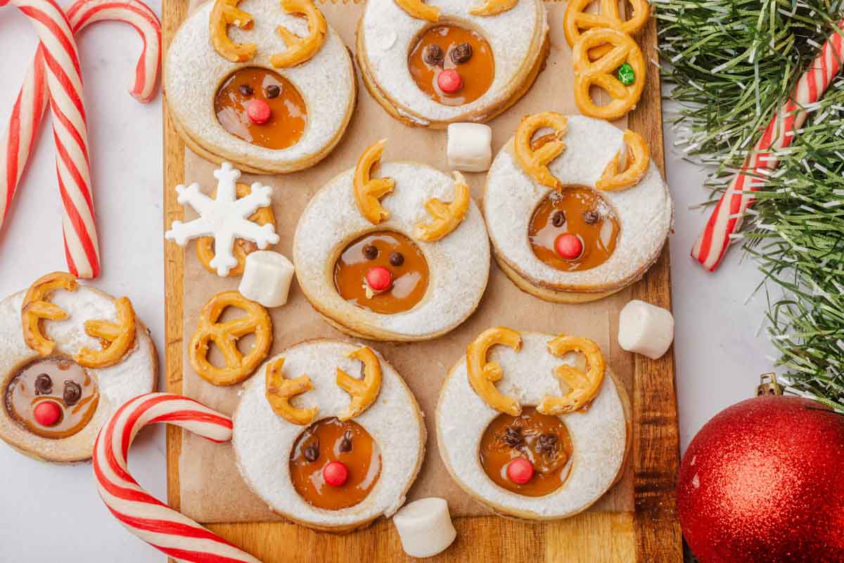 landscape photo of 6 reindeer linzer cookies on wooden board with candy canes and holiday decorations