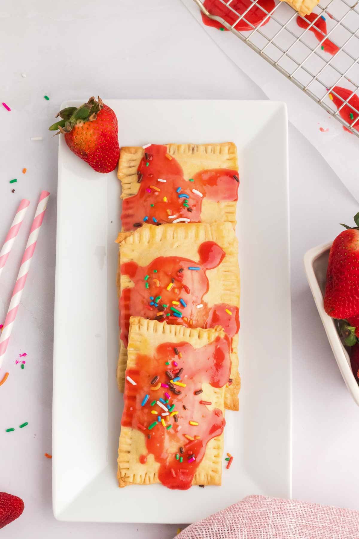 three strawberry pop tarts on a white plate with a fresh strawberry