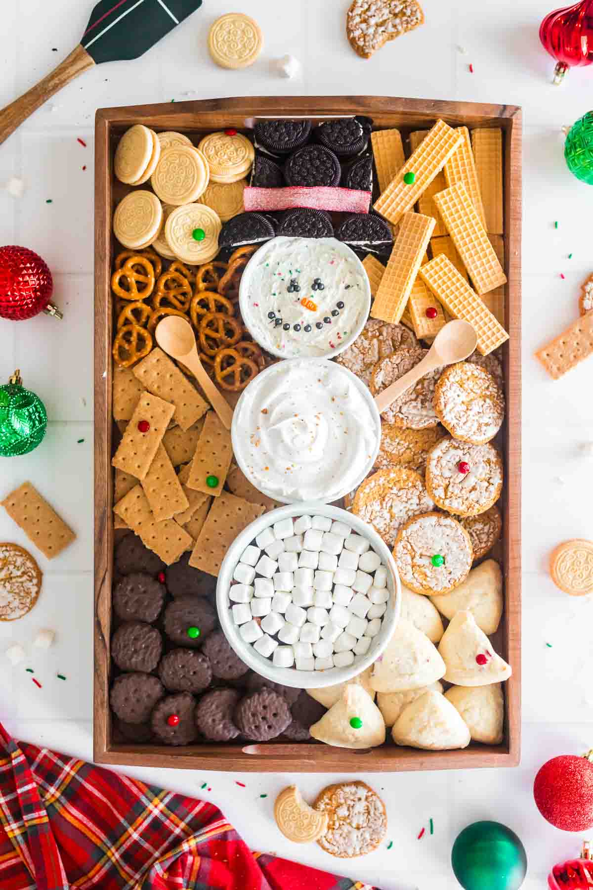 Frosty snowman dessert dip board with cookies and dippers surrounding it on a wooden tray