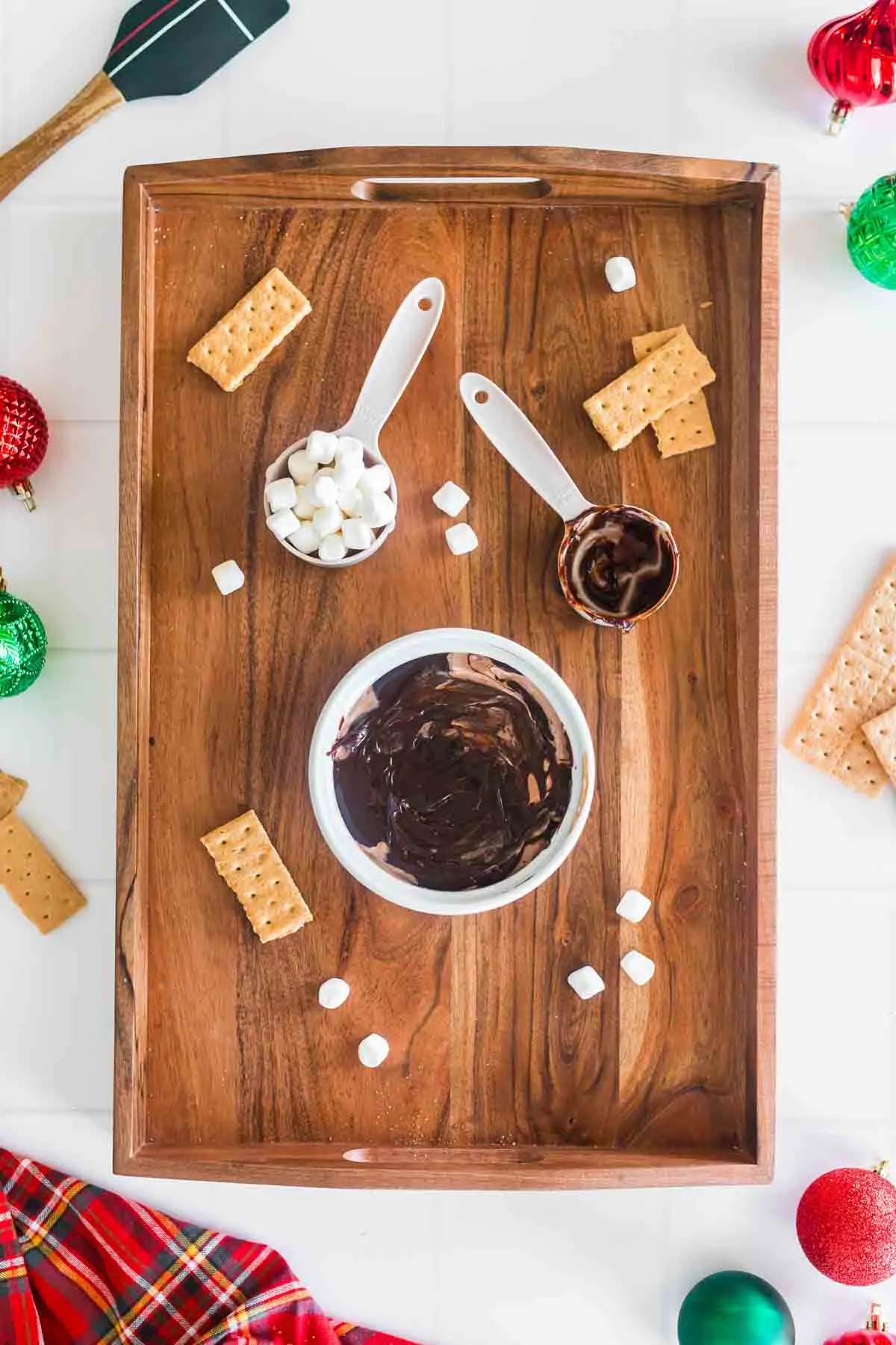 hot chocolate dip in white ramekin covered in hot fudge with a measuring cup of mini marshmallows on wooden tray