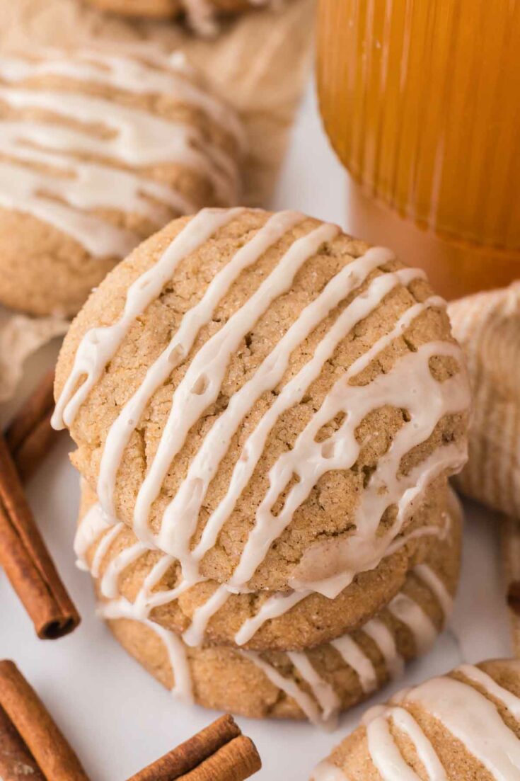 stacked apple cider cookies with icing and cinnamon sticks.