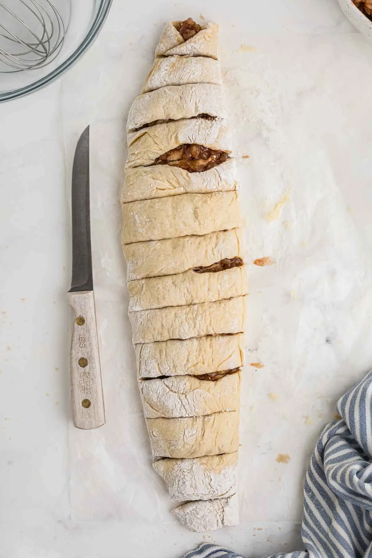 sliced apple pie filled dough into rolls in log with a knife.