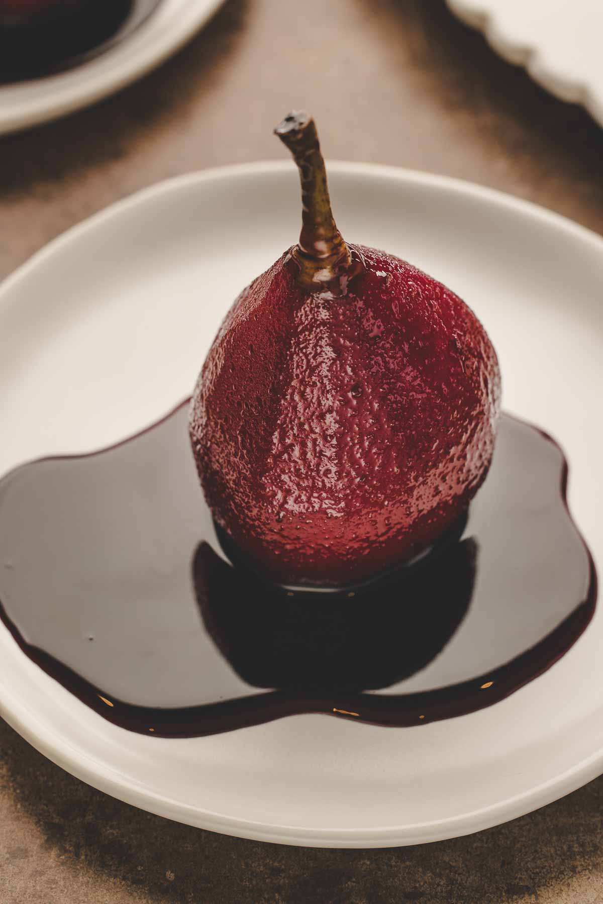 red wine poached pear with extra reduction sauce on white plate.