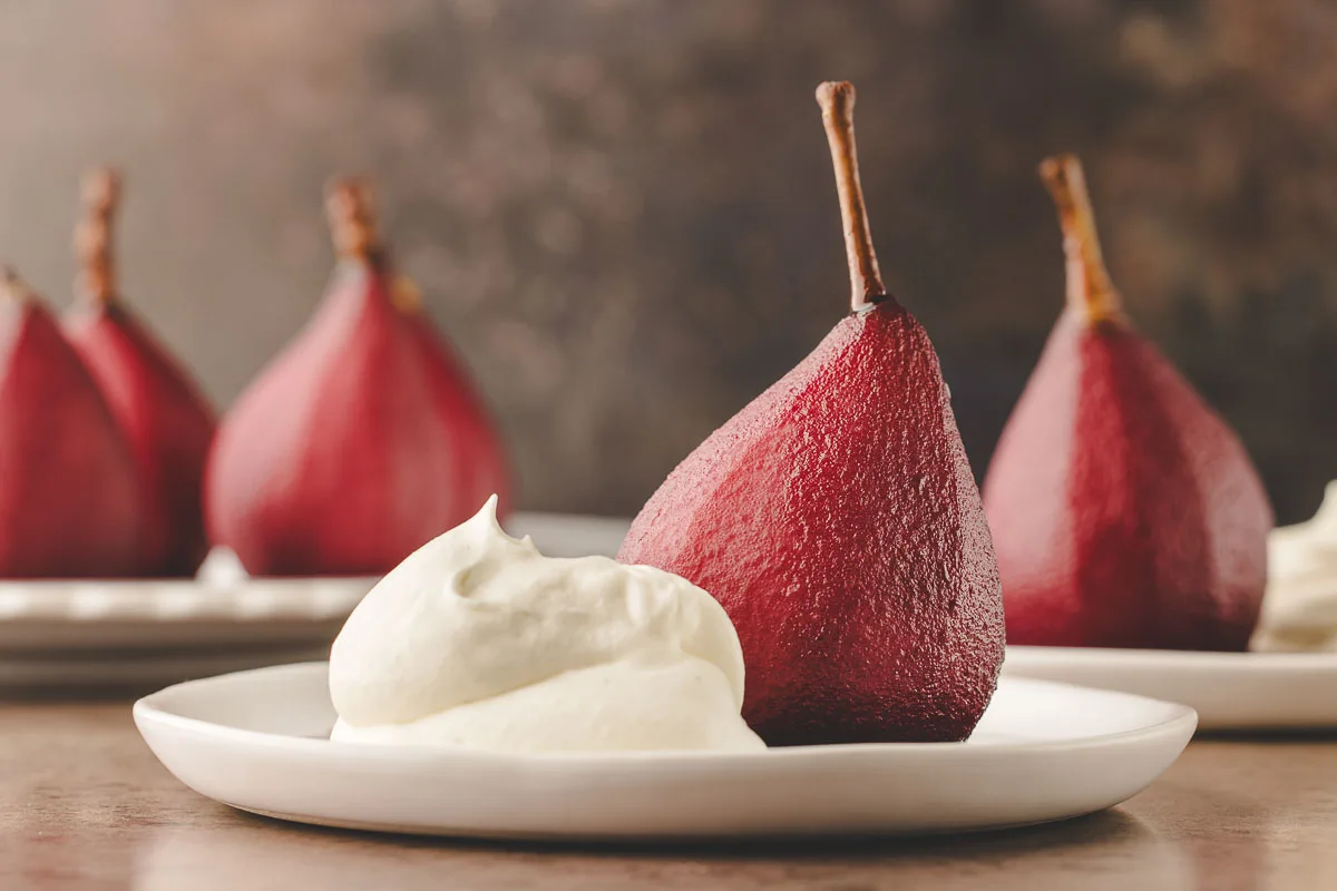 landscape picture of red wine poached pears and a dollop of whipped mascarpone cream on white plate.