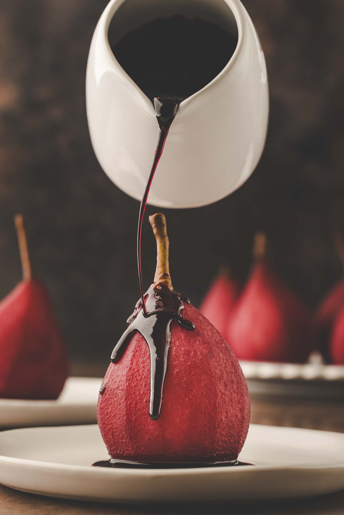 pouring red wine reduction sauce over poached pear.