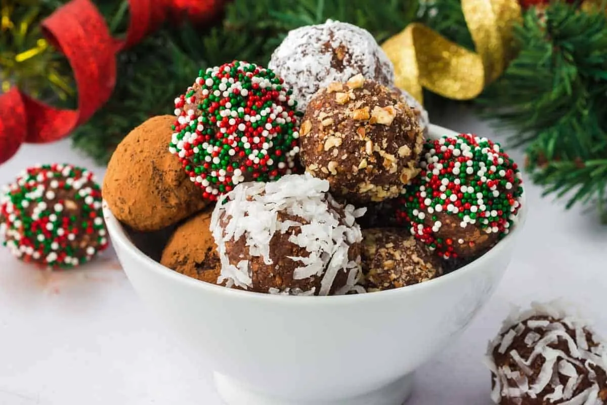 Chocolate Rum Balls with different toppings in a white bowl and Christmas decorations.