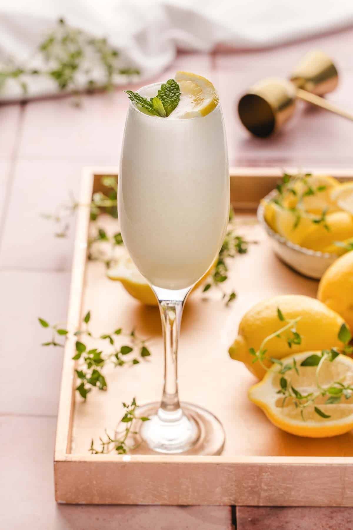 Sgroppino Cocktail on gold tray with lemons and herbs.